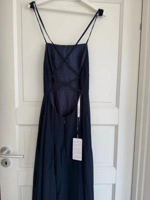 Marinblå balklänning med öppen rygg - Superfin marinblå balklänning från JJ's House med smala axelband och öppen rygg. Klänningen har en slits och knytning i ryggen och sitter som en smäck. Perfekt inför kommande bal eller festligheter. Klänningen är oanvänd och prislappen är kvar. Säljer klänningen då den inte hann komma fram innan min bal. 