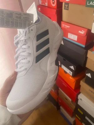 Vita Adidas sneakers med svarta ränder - Snygga vita sneakers från Adidas med klassiska svarta ränder på sidan. Skorna har en låg profil och är tillverkade i meshmaterial med detaljer i syntet. Perfekta för dig som vill ha en sportig och stilren look.