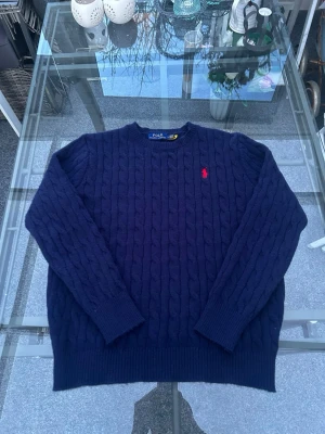 Polo Ralph Lauren cable knit sweater navy – M - Säljer en klassisk Polo Ralph Lauren cable knit i navy med röd broderad polo-logga. Tidlös preppy / old money-stil som passar perfekt till jeans, chinos eller över en skjorta.  • Märke: Polo Ralph Lauren • Storlek: M • Färg: Navy blå • Material: 100% bomull • Skick: Mycket fint skick  En riktig klassiker från Ralph Lauren som aldrig går ur stil. Perfekt om du gillar preppy, vintage eller clean streetwear.
