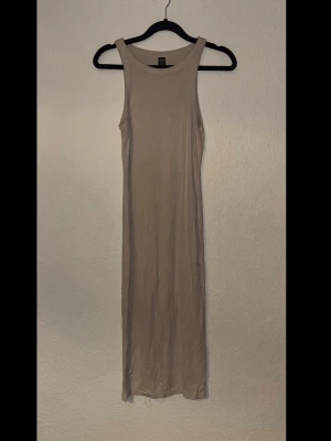 Beige ribbad långklänning - En enkel och stilren beige långklänning. Klänningen är ribbad, ärmlös och har en rak passform med breda axelband. Perfekt för en avslappnad och trendig look.