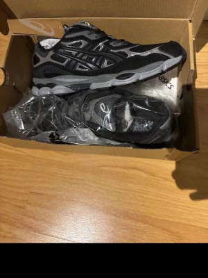 Svarta och grå ASICS sneakers - Snygga ASICS GEL-NYC sneakers i svart och grått. Väljer att sälja dessa då de inte riktigt är min stil längre. Skorna är helt oanvända och kommer med boxen. 