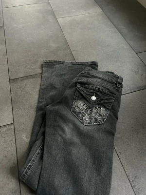 Grå jeans med broderad ficka Gina Tricot - Snygga grå jeans från Gina Tricot med unik broderad bakficka och knappdetalj. Jeansen har klassisk femficksmodell och raka ben. Perfekta för dig som vill ha något extra till din outfit.
