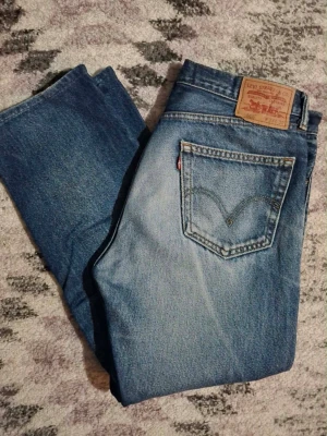 Levi's 505 blå jeans W34 L30 - Klassiska blå Levi's 505 jeans med rak passform och femficksdesign. Jeansen har en ljus tvätt på framsidan och tydlig Levi's-lapp bak i midjan. Tillverkade i slitstark denim med den ikoniska röda Levi's-taggen på bakfickan.