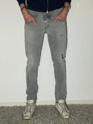 Grå dondup jeans med schyssta slitningar skinny fit - Säljer ett par grå skinny jeans med slitningar och distressed detaljer. Jeansen har klassisk femficksmodell, dragkedjegylf och smal passform. Perfekta för en avslappnad och trendig look.