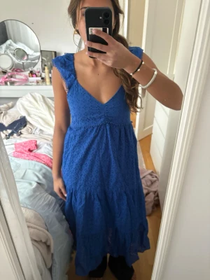 Blå sommarklänning med volangärmar - Söt blå klänning med broderade detaljer och volangärmar. Djup V-ringning och lätt utställd kjol ger en luftig känsla.