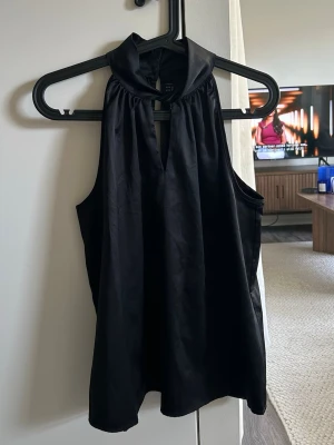 Svart ärmlös halterneck topp - Snygg svart ärmlös halterneck topp från pieces med hög krage och knapp i nacken. Tunn och mjuk kvalitet som ger ett elegant fall. 🖤