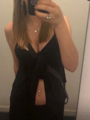 Svart linne med knyt/roset  - Snygg svart linne med knyt framtill och djup v-ringning. Toppen är ärmlös, perfekt för en trendig stil. Passar till både jeans och kjol för en cool look. använd 4 gånger. inga defekter.