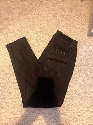 Svarta slim fit jeans från Nudie - Svarta slim fit jeans från Nudie med klassisk femficksdesign och diskret broderad bakficka. Jeansen har normal midja och smal passform, perfekta till en avslappnad stil. Tillverkade i mjukt denimtyg med stretch för extra komfort. Modell: Lean Dean! Otroligt fint skick 