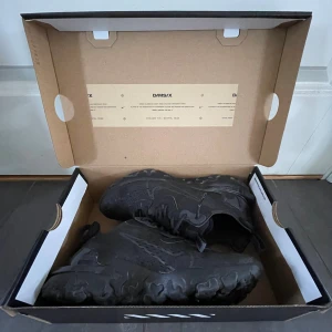 Svarta Nike react sneakers - Säljer ett par helsvarta Nike D/MS/X sneakers med chunky sula och sportig design. Skorna har ventilerande mesh, detaljerade sömmar och reflekterande inslag. Perfekta för dig som gillar en modern och edgy look.