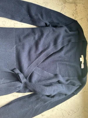 Svart omlottkofta med knytskärp - Mysig svart stickad omlottkofta från Gina Tricot med knytskärp i midjan och breda ribbade muddar. Perfekt för lager-på-lager och enkel att styla till olika outfits.
