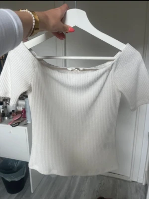 Vit ribbad offshoulder topp - Säljer en vit ribbad topp med offshoulder-design. Toppen är kortärmad och har en snygg, figurnära passform som passar perfekt till jeans eller kjol. Materialet känns mjukt och stretchigt, vilket gör den superbekväm att bära.