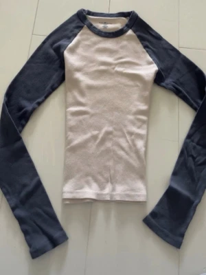 Vit och mörkblå långärmad topp vintage - Snygg långärmad topp med vit kropp och mörkblå ärmar. Klassisk raglanmodell med rund halsringning. Perfekt till jeans eller kjol för en avslappnad look.