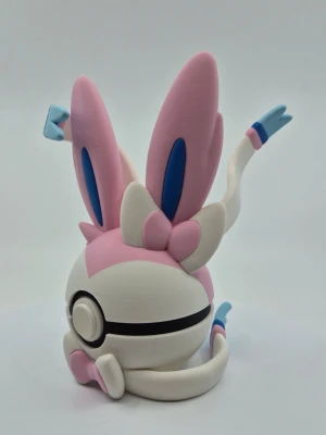 Pokémon pokeball Sylveon - Söt pokeball formad som en Pokéboll med Sylveon-design. Asken är vit, rosa och blå med stora öron och detaljerade band. Tillverkad i plast och har ett lock som öppnas för förvaring av småsaker eller smycken.
