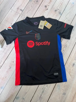 Helt ny - FC Barcelona Lewandowski Nike T-shirt - Säljer helt ny, oanvänd svart FC Barcelona matchtröja från Nike med Lewandowski på ryggen. T-shirten är i superbra skick och har som sagt aldrig används. Säljer pga att jag köpte fel storlek. Perfekt för dig som älskar fotboll och Barca.