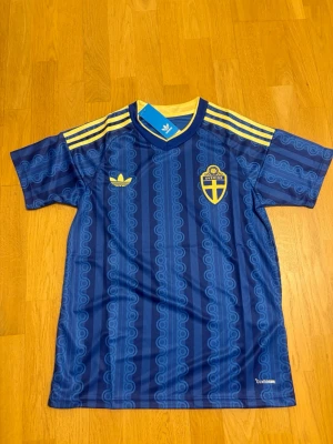 Sveriges vm tröja M - Snygg blå fotbollströja från Adidas med Sveriges landslagsemblem på bröstet och gula detaljer. Tröjan har korta ärmar, V-ringning och gula ränder på axlarna. Tillverkad i lätt och ventilerande material med Climalite-teknologi.