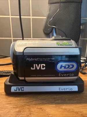 JVC Everio HDD videokamera - Säljer en JVC Everio videokamera med hårddisk, silver och svart design. Kameran har 40GB lagring, 2.0 megapixel sensor och F1.2 asfäriskt objektiv. Utrustad med handrem och laddningsstation. Perfekt för att spela in både video och stillbilder. Nyskick saknas bara låda väska till kameran fås med! Dm vid frågor 