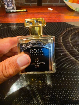 Roja Parfums 18 Burlington 19 EdP - Lyxig parfym från Roja Parfums, 18 Burlington 19. Flaskan är fyrkantig i genomskinligt glas med svart och guld etikett samt en exklusiv guldig kork med diamantmönster. Parfymen har en elegant och modern design som sticker ut i parfymhyllan.
