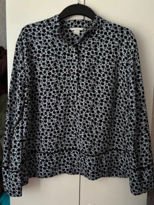 Blommig svartvit blus med krage - Blus med svartvitt blommönster och liten krage från H&M i storlek 40. Blusen har långa ärmar och en lös, avslappnad passform!