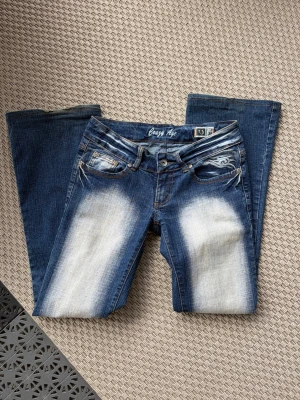 Blå bootcut jeans från Crazy Age - Säljer ett par blå bootcut jeans från Crazy Age med slitna detaljer och ljusa partier framtill. Jeansen har klassisk femficksmodell, låg midja och kontrastsömmar. Skriv för fler frågor och prisförslag 