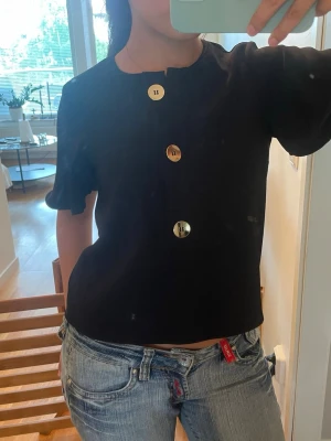 Svart blus med stora knappar - Stilren svart blus med tre stora, blanka knappar framtill. Man kan välja att ha en rundad krage eller vika in sidorna för en v ringad look!!