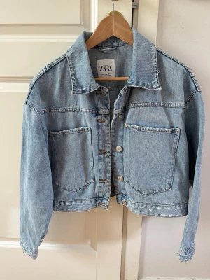 Ljusblå jeansjacka från Zara - Trendig ljusblå jeansjacka från Zara med oversized passform och stora bröstfickor. Klassisk krage, knappstängning framtill och avslappnad look. Perfekt att slänga över en hoodie eller t-shirt för en cool vibe.