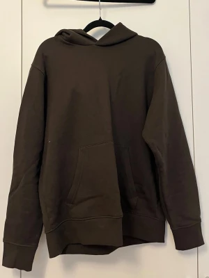 Mörkbrun hoodie med magficka - Mango man  - En enkel och stilren mörkbrun hoodie med huva och stor magficka framtill. Hoodien har långa ärmar och ribbade muddar vid ärmslut och nederkant. Perfekt för en avslappnad look och passar till det mesta i garderoben.
