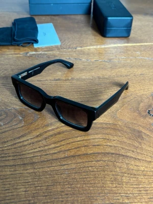 Chimi 05 core ”black” - Säljer ett par stilrena svarta solglasögon från Chimi med breda bågar och fyrkantig form. Glasen är mörka och ramen är i blank plast som ger en modern vibe. Perfekta för dig som vill ha en edgy och trendig look. Använda fåtal gånger i nyskick. 