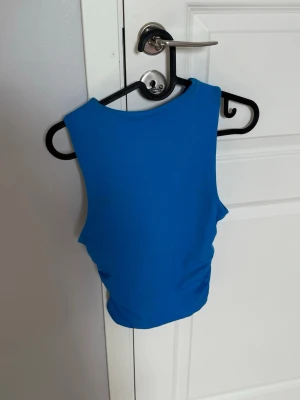 Blå cropped tanktop - Säljer en blå cropped tanktop i stretchigt material. Modellen är ärmlös med hög halsringning och tight passform, perfekt för att styla med jeans eller kjol. Enkel och stilren design utan tryck eller detaljer.