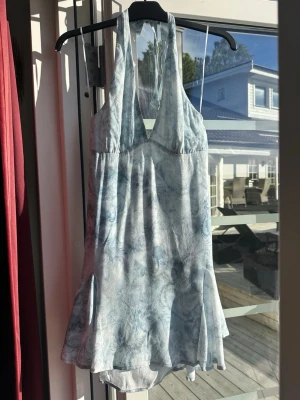 Ljusblå halterneck kortklänning ifrån Bershka.  - Säljer en ljusblå kortklänning med halterneck och v-ringning. Klänningen har ett mjukt, flygigt tyg och ett subtilt  paisleymönster i blå toner. Perfekt för varma dagar och har en lätt volang nedtill för extra rörelse. Superfin! Helt ny med lapp kvar! 