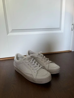 Vita låga sneakers från Crime London - Stilrena vita sneakers från Crime London i lågt snitt. Tillverkade i slätt läder med klassisk siluett, vita skosnören och diskret silverfärgad numrering på sidan. Skorna ska de använda ut redan från start då de e så de e designade. Perfekta för en clean och modern look.