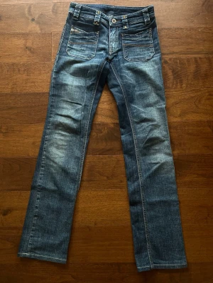 Lågmidjade mörkblå jeans - Lågmidjade blå raka jeans från Diesel med slitningar och kontrastsömmar. Klassisk femficksmodell med logotyp på myntfickan och detaljerade nitar. Jeansen är min mammas gamla och är försmå på mig därav inga bilder med jeansen på.