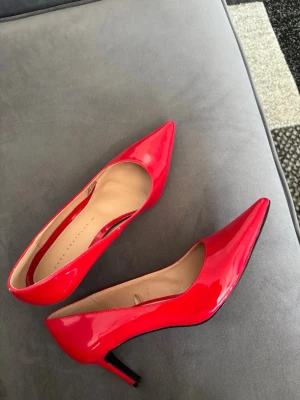 Röda lackpumps med klassisk siluett - Snygga röda pumps i lackmaterial med spetsig tå och smal klack. Skorna har en klassisk siluett och en elegant finish som verkligen sticker ut. Perfekta för dig som vill ha ett par statement-heels till din outfit.