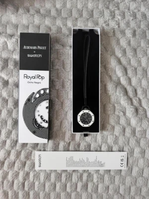 Swatch x Audemars Piguet Royal Pop klocka - Unik Swatch x Audemars Piguet Royal Pop Ocho Negro klocka med svart urtavla och vita detaljer. Klockan har en rund form och levereras i originalförpackning med svart band. Perfekt för dig som gillar coola och moderna accessoarer.