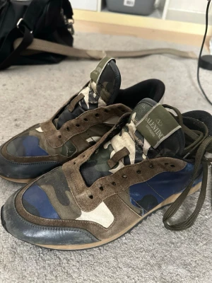 Valentino rockrunners bra pfis vid snabba affärer - Säljer ett par snygga sneakers från Valentino med camomönster i grönt, blått, beige och svart. Skorna har detaljer i mocka och textil samt gröna skosnören. Tungan har Valentino-logga och sulan är i gummi. Perfekta för dig som gillar streetwear och vill sticka ut.