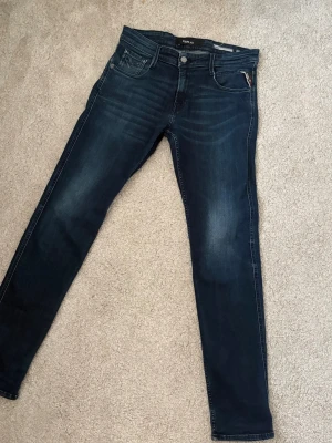 Replay  - Snygga mörkblå skinny jeans från Replay med klassisk femficksmodell och diskreta slitningar framtill. Jeansen har en smal passform och är tillverkade i stretchigt denimtyg för extra komfort. Märkespatch bak i midjan och silverfärgade detaljer.