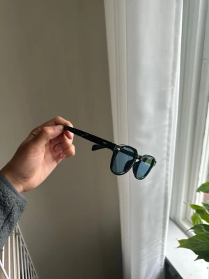 Svarta solglasögon med blåtonade glas - Solglasögon med svart, rundad båge och blåtonade glas. Klassisk och stilren design som passar till många outfits. 