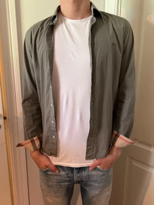 Burberry skjorta - Stilren skjorta från Burberry Brit i beige och svart med klassiskt rutigt mönster på insidan av kragen. Tillverkad i mjuk bomull som känns skön mot huden. Perfekt för dig som vill ha en tidlös och ikonisk look.