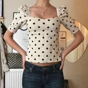 Prickig topp  - Supersöt topp från H&M med puffärmar och fyrkantig ringning. Vit botten med stora svarta prickar ger en retrovibe. Toppen är figurnära och har korta ärmar som ger en trendig look. Perfekt att styla med jeans eller kjol.
