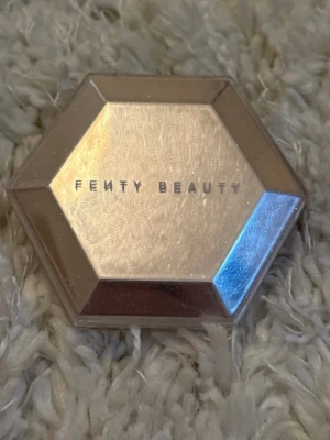 Fenty Beauty Diamond Bomb Bronzer - Fenty Beauty Diamond Bomb Bronzer i nyansen 'How Many Carats?!'. Kommer i en sexkantig, metallic-roséguldig dosa. Produkten har ett intensivt silverskimrande glow och innehåller 8g. Perfekt för dig som vill ha extra lyster till din makeup.
