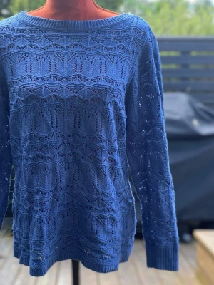 Blå stickad tröja med mönster 42 - Säljer en blå stickad tröja med lång ärm och rund halsringning. Tröjan har ett detaljerat hålmönster över hela plagget och ribbade muddar vid ärmslut och nederkant. Blå långärmad tröja Akryl Längd: 52 cm Bystvidd: 50 cm  Inga bilder på mig! Katter finns i hemmet!