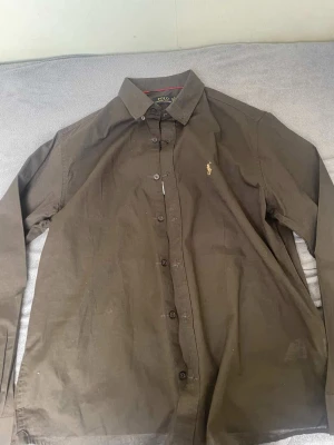 Brun skjorta från Polo Ralph Lauren - Snygg brun skjorta från Polo Ralph Lauren med klassisk krage och knappar framtill. Aldrig använt.  Perfekt för dig som gillar stilrena plagg med en tidlös känsla.