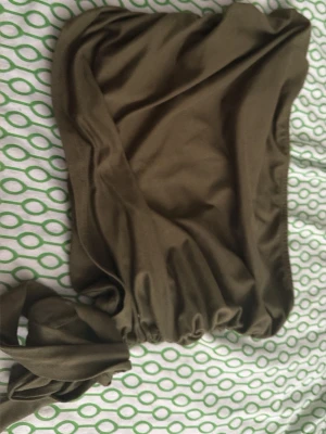 Olivgrön bandeau topp med knyt - Trendig olivgrön bandeau topp i mjukt stretchigt tyg. Toppen har en snygg knytning i sidan som ger en cool detalj och sitter uppe med resår. Perfekt till sommaren och enkel att styla med jeans eller kjol.