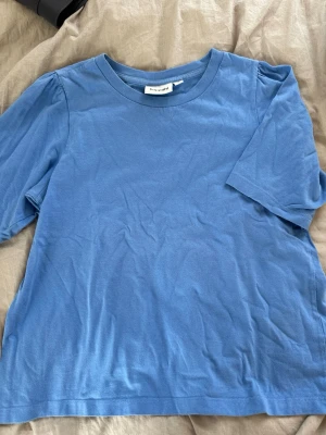 Blå t-shirt från Kappahl  - En enkel blå t-shirt från Kappahl med rund halsringning och korta ärmar. Tillverkad i mjuk bomull och har en avslappnad passform med foffiga armar. 