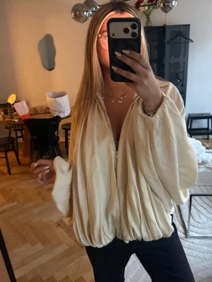 Beige oversized jacka med ballongärm - Säljer en beige oversized jacka med ballongärmar och dragkedja framtill. Jackan har en unik, puffig siluett och är tillverkad i ett glansigt material som ger en lyxig känsla. Perfekt för dig som vill sticka ut med en trendig och cool look.