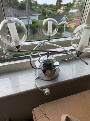 Kromad taklampa med glaskupor - Säljer en snygg taklampa i kromad metall med tre runda, genomskinliga glaskupor. Lampan har en modern, böjd design och vit sladd med stickkontakt. Perfekt för dig som vill ha något unikt till rummet.
