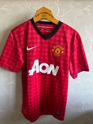 Manchester United matchtröja Nike - Röd Manchester United matchtröja från Nike med svart V-ringning och rutmönster. Tryck med klubbmärke, sponsorlogga och spelarnamn Anderson samt nummer 8 på ryggen. Tillverkad i lätt och ventilerande Dri-FIT material, perfekt för fotbollsträning eller match.