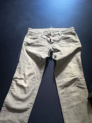 Gråa jeans dsquared - Säljer ett par gråa dsquared  jeans med coola slitningar och detaljer på benen. Jeansen har klassisk femficksdesign och raka ben. Perfekt för dig som gillar en avslappnad och trendig look