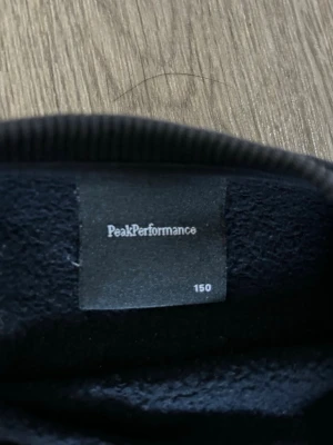 Mörkblå sweatshirt Peak Performance - Snygg mörkblå sweatshirt från Peak Performance med vit logga på bröstet. Tröjan har rund halsringning, långa ärmar och ribbade muddar vid ärmslut och nederkant. Perfekt för en avslappnad och sportig stil.