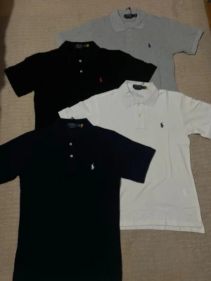 Klassiska pikétröjor från Ralph Lauren  - I am selling 4 brand-new, unused Ralph Lauren polo shirts. The price listed is for all 4 together. Individually, I sell them for 399 SEK each. For a quick and smooth deal, we may be able to agree on a better price.  * Black polo with red logo: 399 SEK * White polo with navy logo: 399 SEK * Grey polo with navy logo: 399 SEK * Navy polo with white logo: 399 SEK  All four together: 1,449 SEK  Size: S, Slim Fit. The original tag string is still attached.  If you have any questions, feel free to send