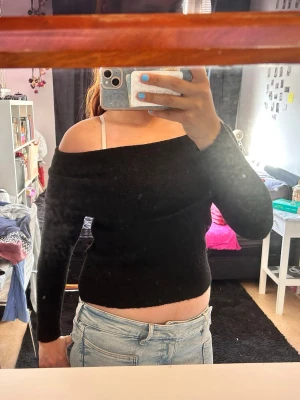 Svart off shoulder stickad tröja - Säljer en svart stickad tröja med off shoulder-design och långa ärmar. Tröjan har en bred krage som vilar över axlarna och är gjord i ett mjukt, stretchigt material. Perfekt för dig som vill ha en trendig och bekväm look.